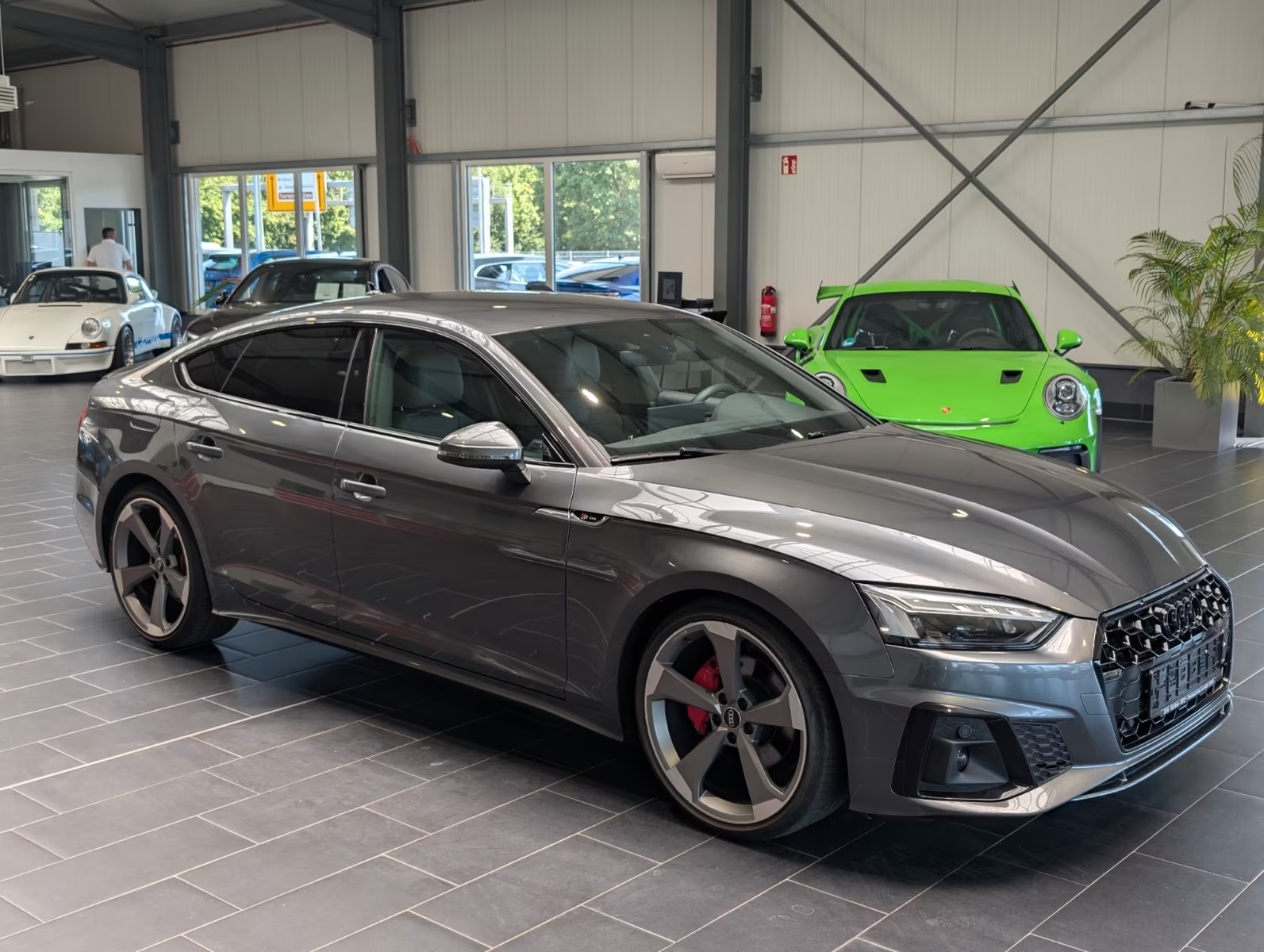 Front three-quarter view of the grey metallic Audi A5 Sportback from the passenger side, showing the side profile and alloy wheels.