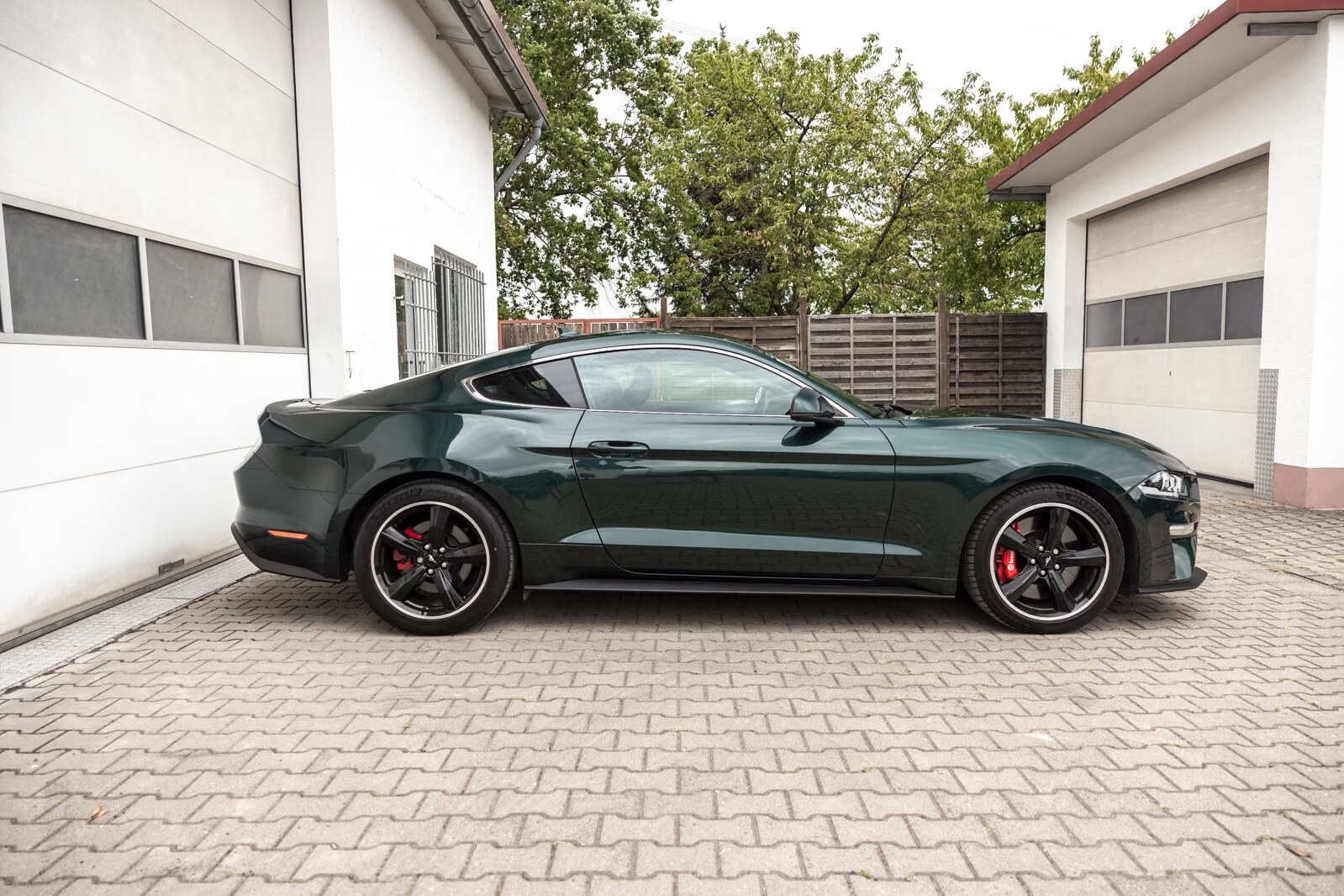Passenger-side profile of the green Ford Mustang Bullitt on a paved forecourt.