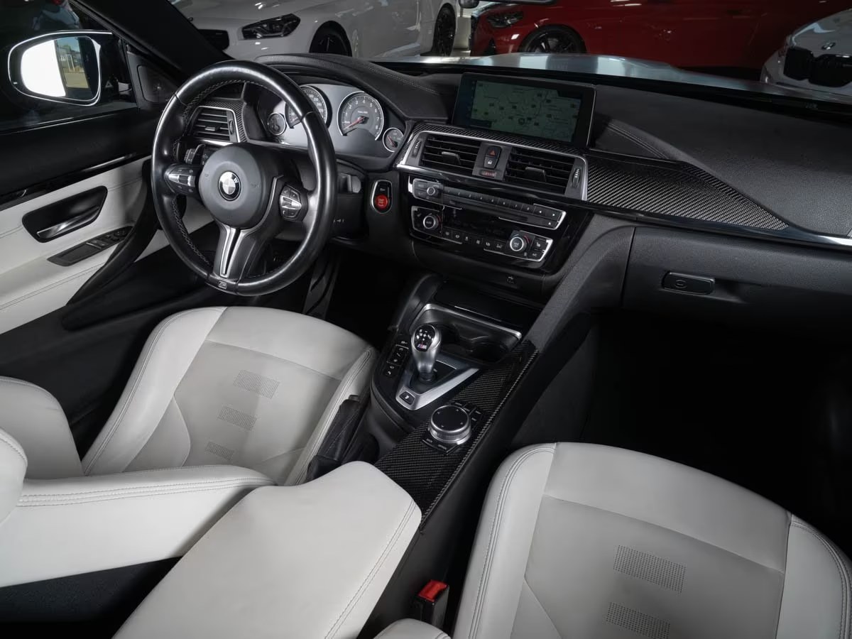 Wide interior view of the BMW M4 dashboard, navigation screen and Opal White leather seating.