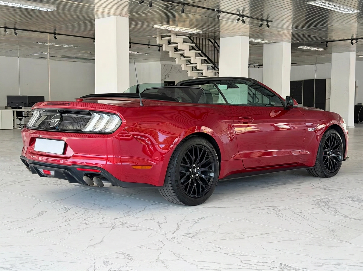 Red Ford Mustang GT Convertible in a showroom, rear three-quarter view with the roof closed.