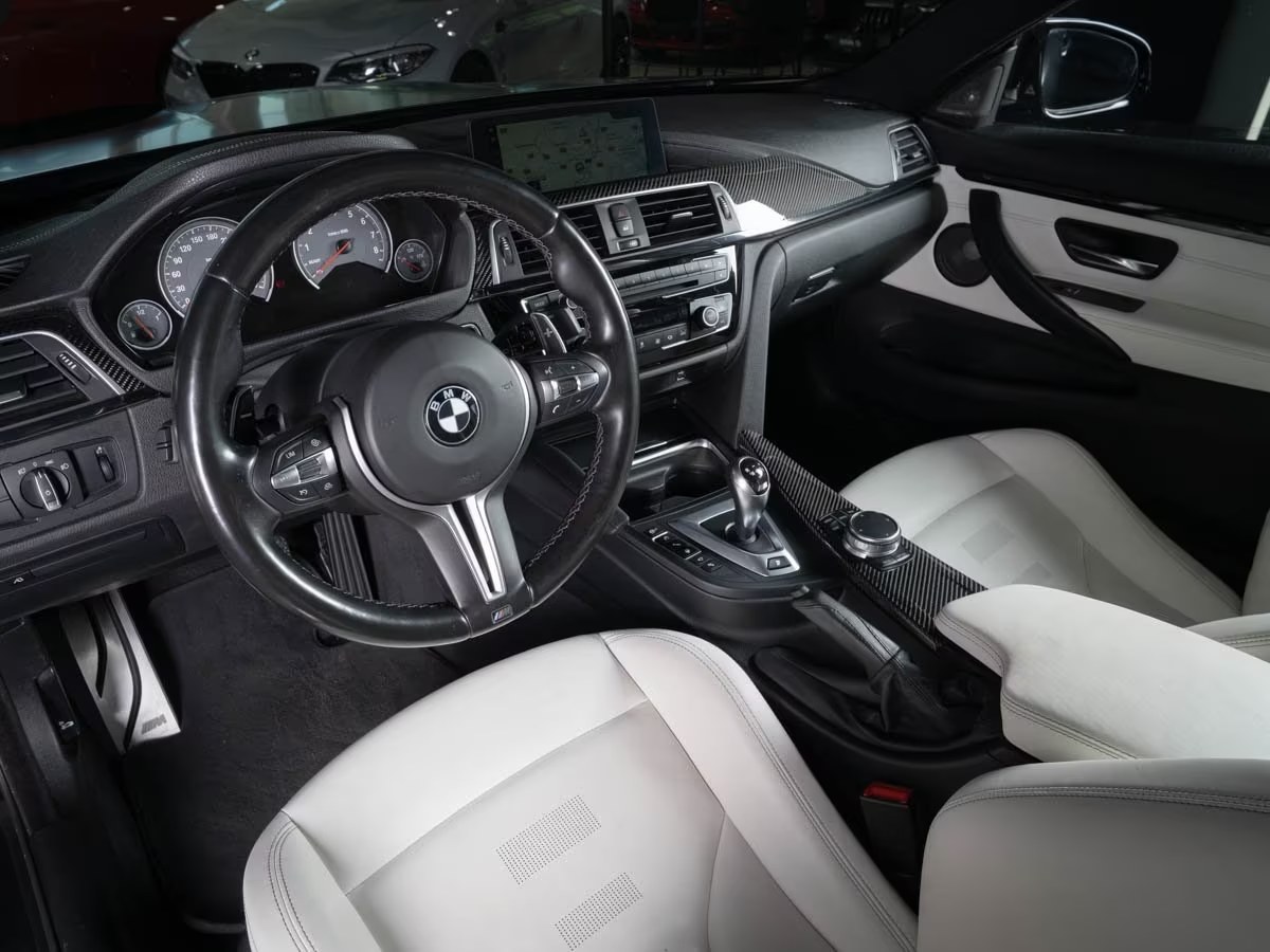 Driver's side cockpit of the BMW M4 with M steering wheel, carbon trim and Opal White leather seats.