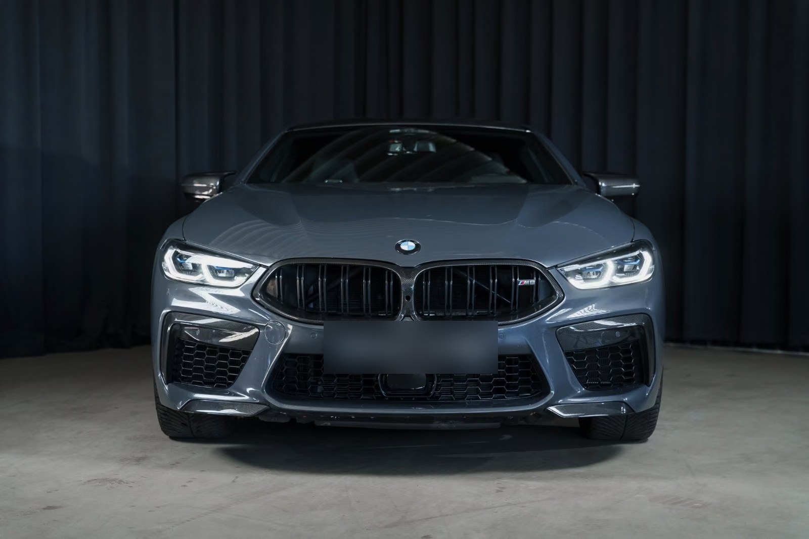 Head-on front view of the grey BMW M8 Coupé showing the carbon kidney grille and laser headlights.