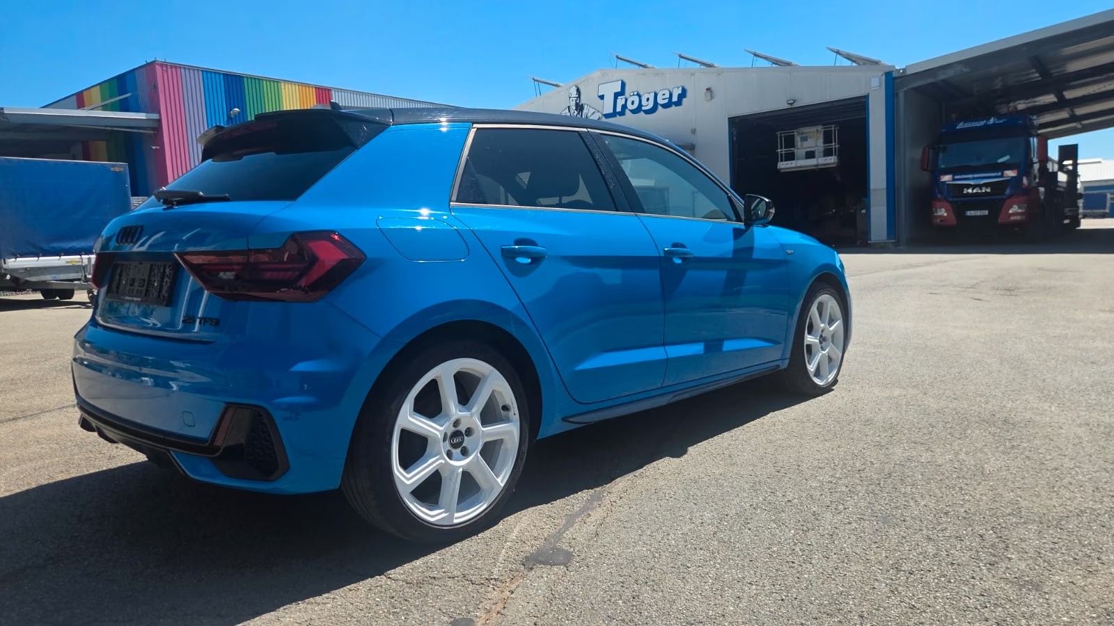 Rear three-quarter view of the blue Audi A1 Sportback showing the tailgate, rear lights and roof spoiler.