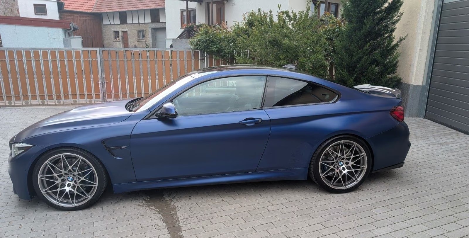 Side profile of the matte blue BMW M4 Competition with star spoke 666 wheels.