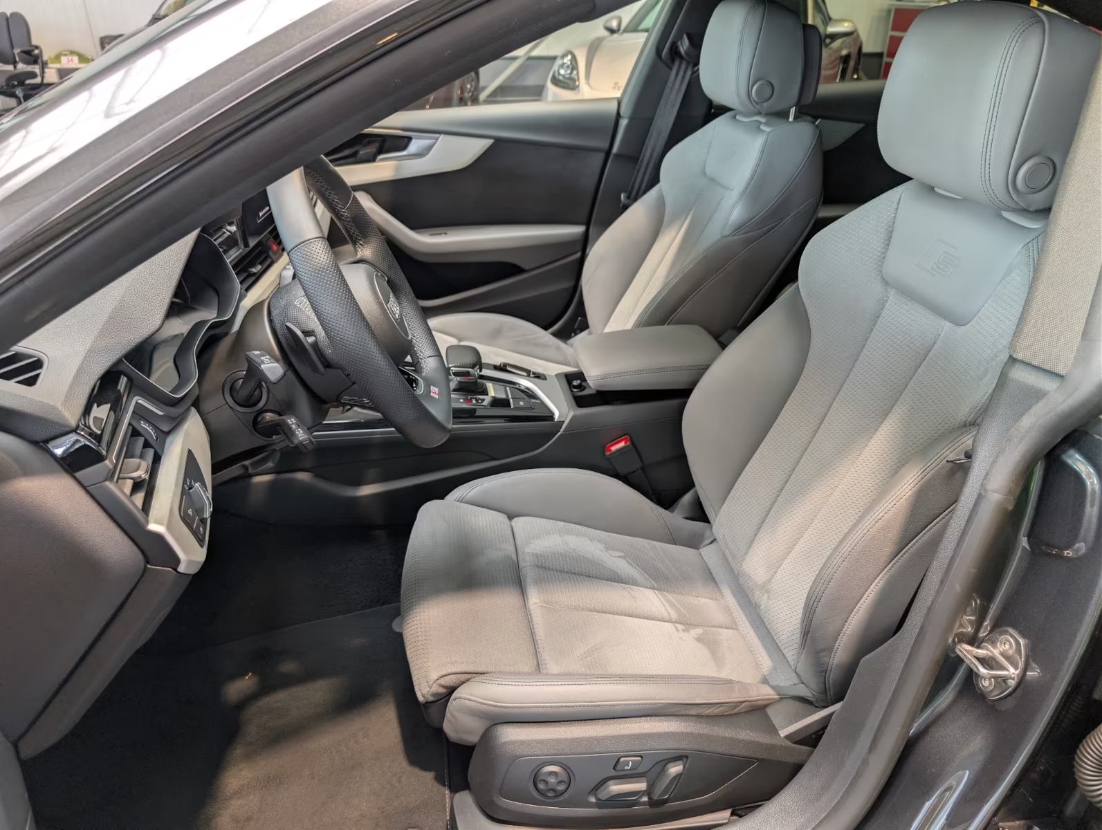 Driver-side interior of the Audi A5 Sportback showing the sport seats, steering wheel and centre console, viewed through the open front door.