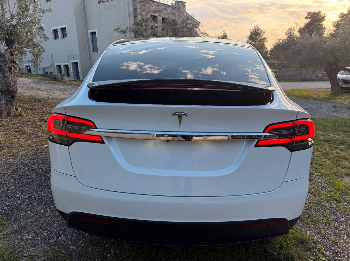 Rear view of the white Tesla Model X with carbon spoiler at sunset.