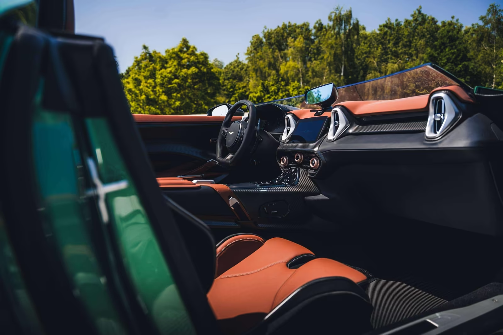 Side view into the DBR22 cabin showing the dashboard, screen and tan leather seats under open sky.