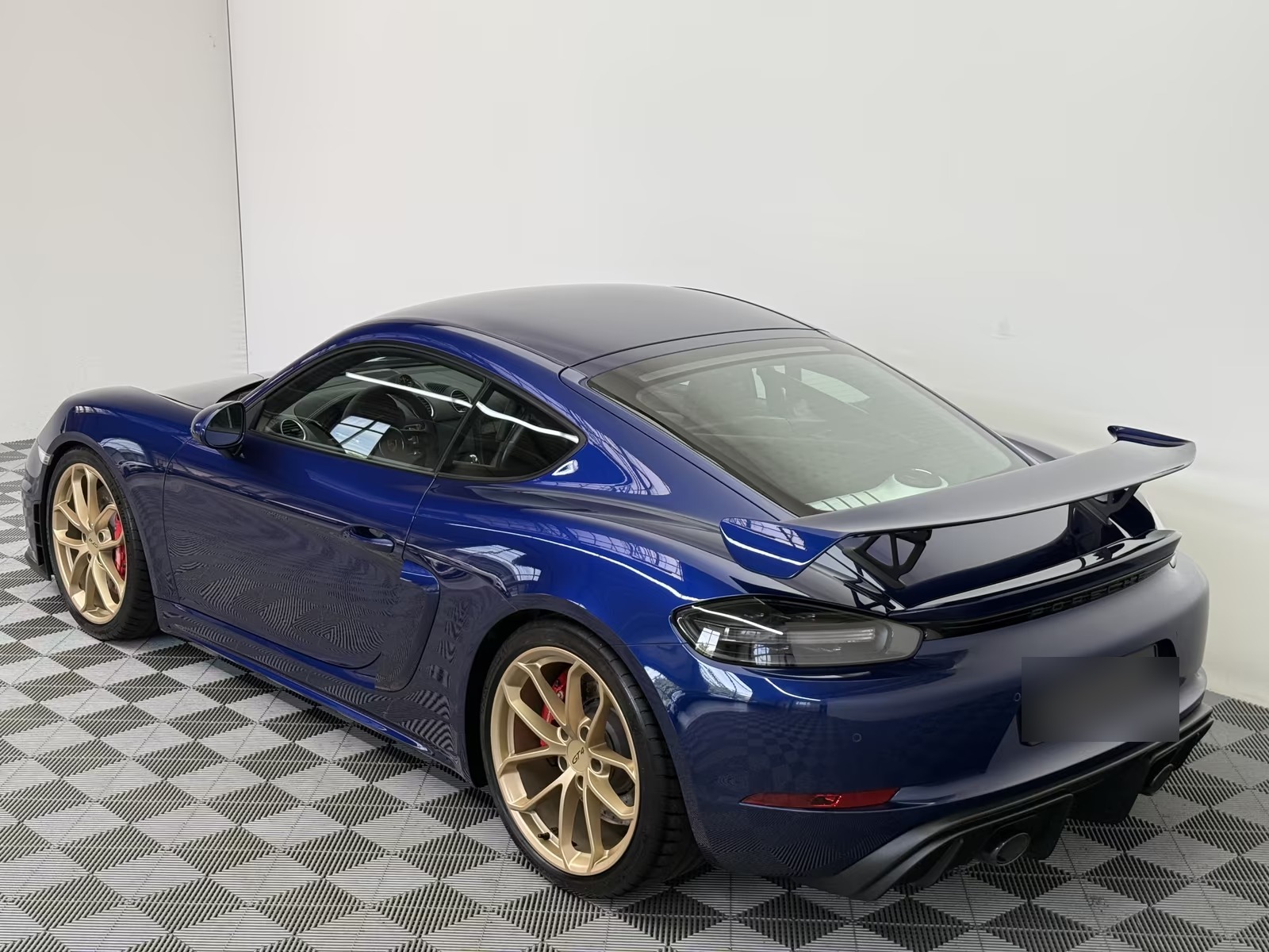 Rear three-quarter view of the blue Porsche 718 Cayman GT4 showing the fixed rear wing, darkened LED rear lights and rear diffuser.