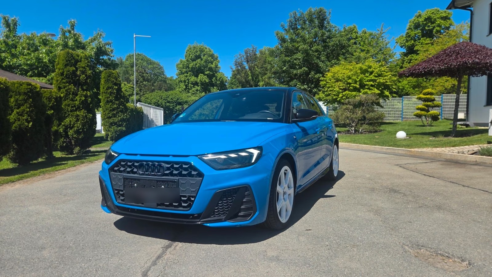Blue Audi A1 Sportback S line, front three-quarter view from the driver side on a sunny driveway.