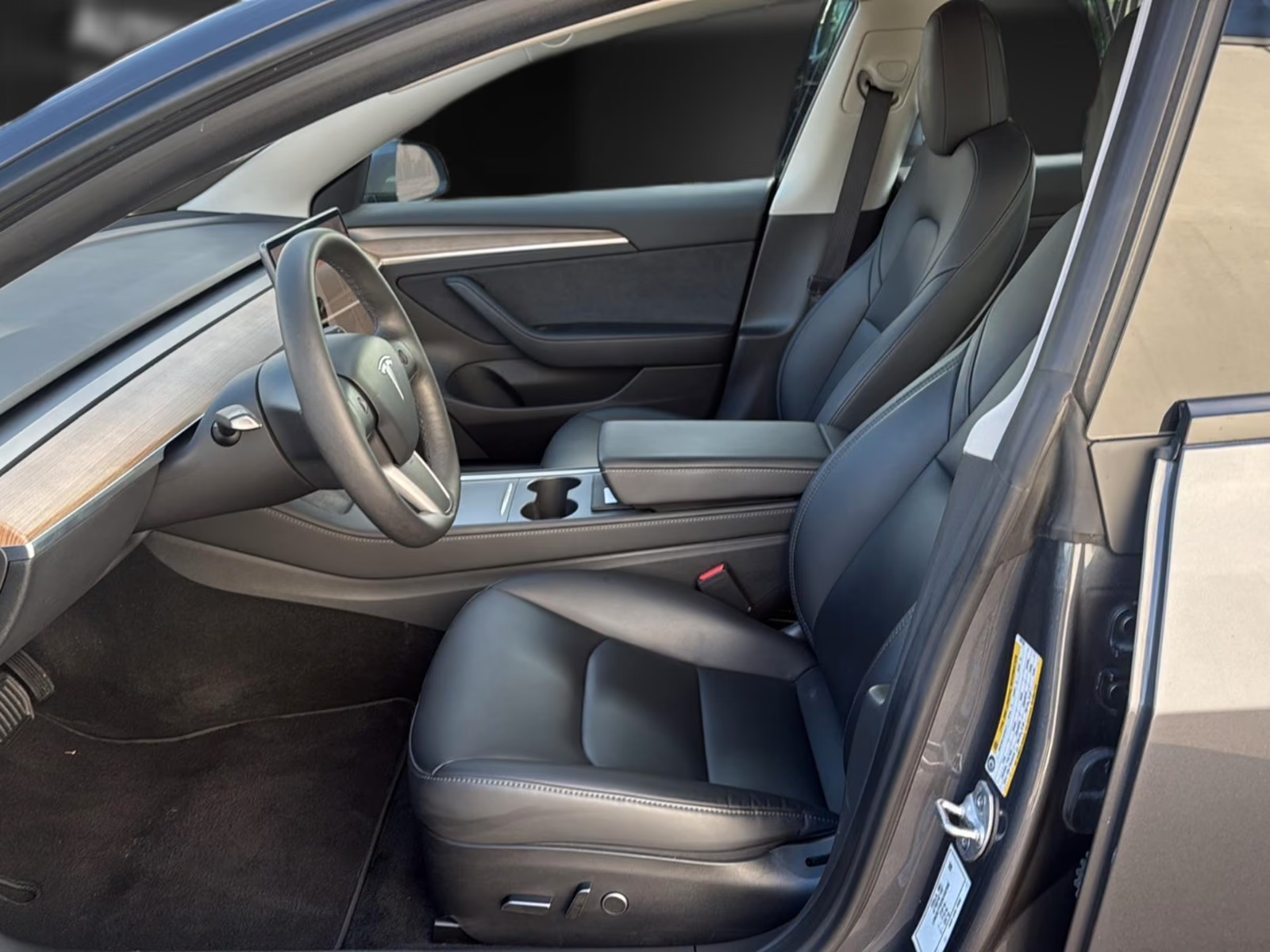 Driver's side interior of the Tesla Model 3 with open door and electrically adjustable seat.