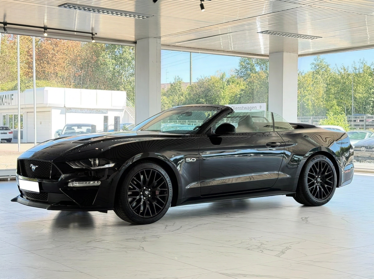 Black Ford Mustang GT Convertible in a showroom, front three-quarter view with the roof open.