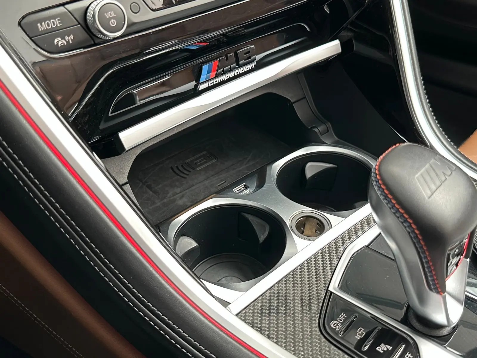 Centre console storage of the BMW M8 showing the M8 Competition badge, wireless charging tray and cup holders.