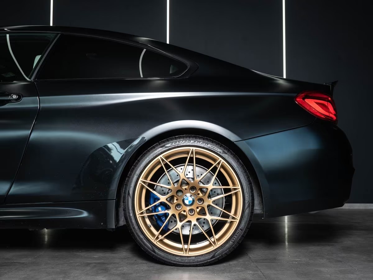 Rear wheel detail of the BMW M4 showing the gold star-spoke wheel and blue M brake caliper.