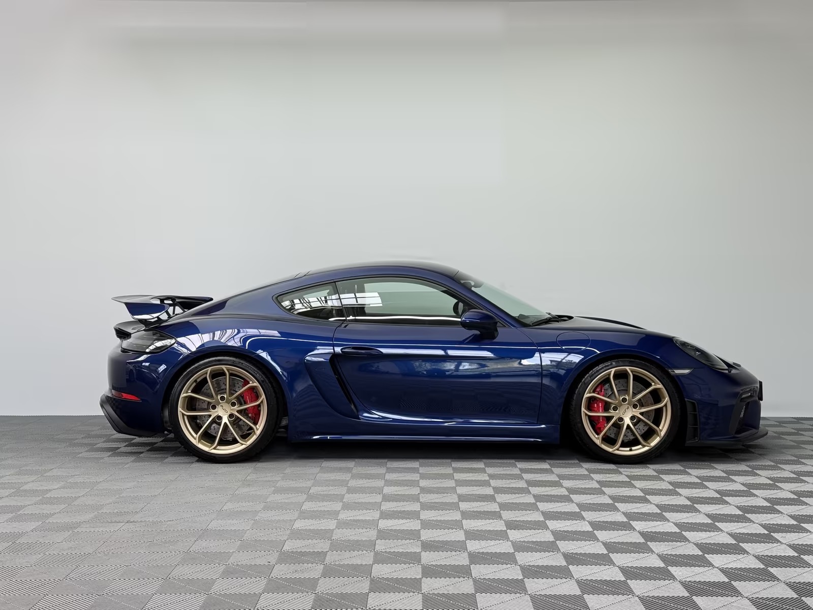 Side profile of the Porsche 718 Cayman GT4 from the passenger side showing the low sports suspension and gold wheels.