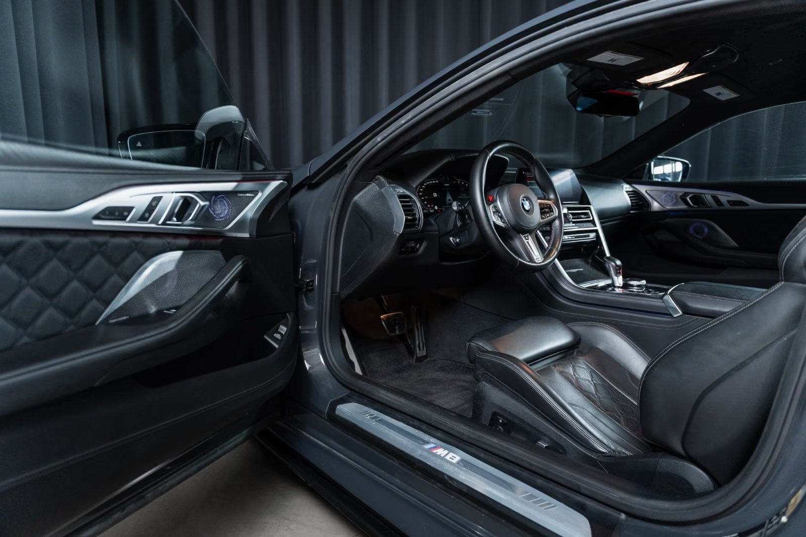 Open driver's door of the BMW M8 showing the black leather cockpit, M steering wheel and M8 door sill.