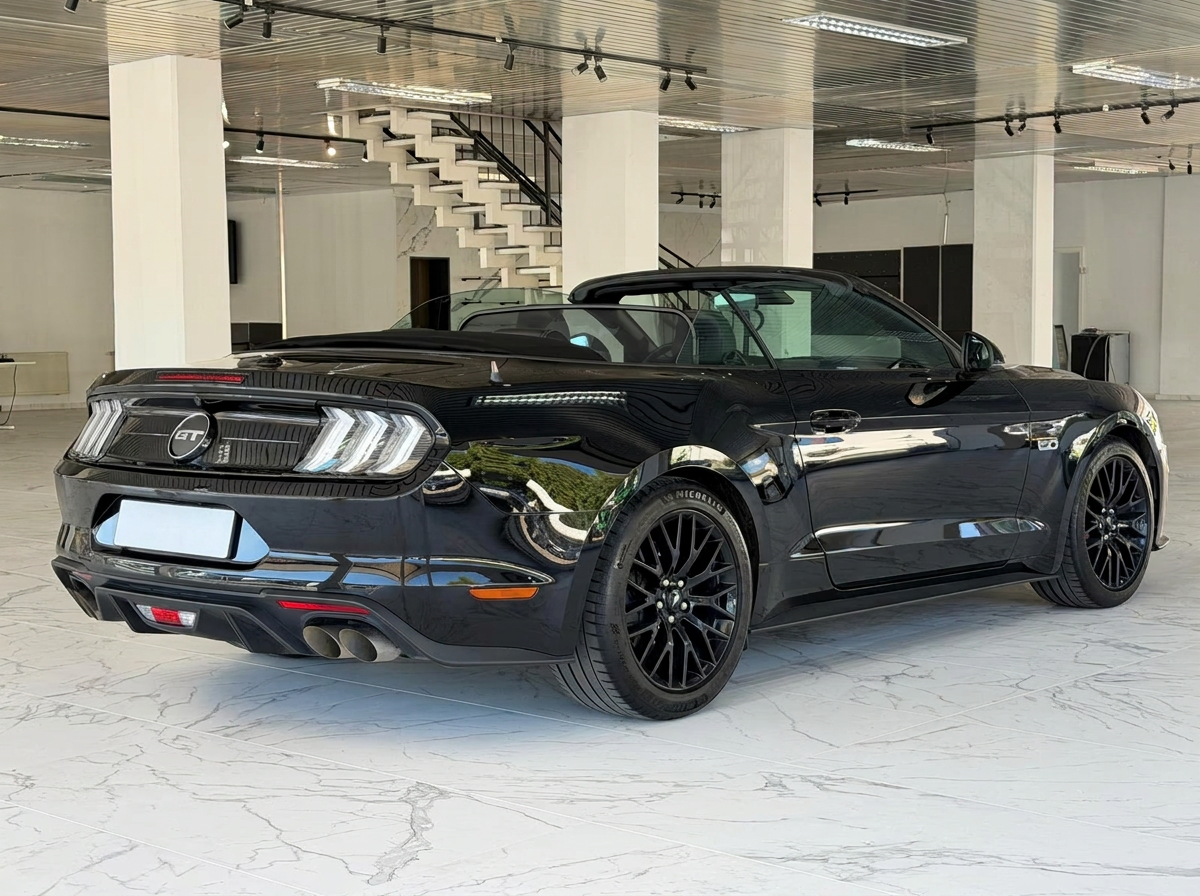 Rear three-quarter view of the black Ford Mustang GT Convertible with its roof open and quad exhaust outlets.