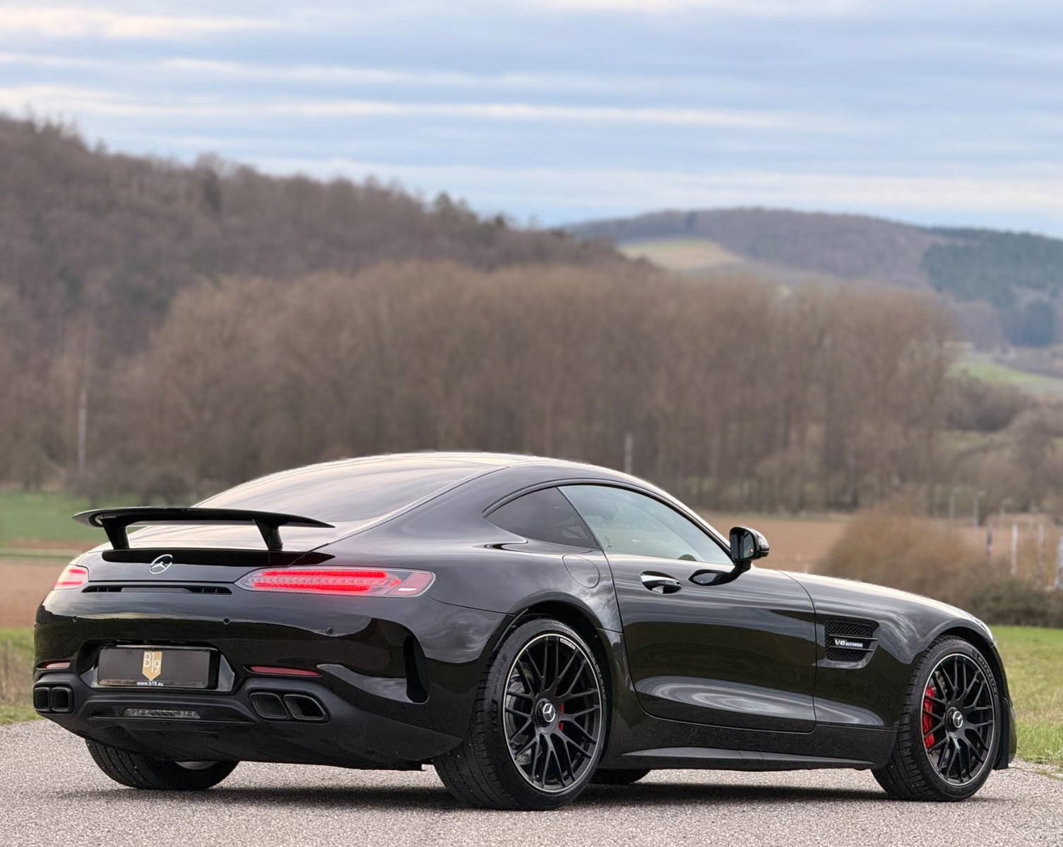 Rear three-quarter view of the black Mercedes-AMG GT C Coupé showing the rear wing, quad exhaust outlets and black AMG forged wheels.