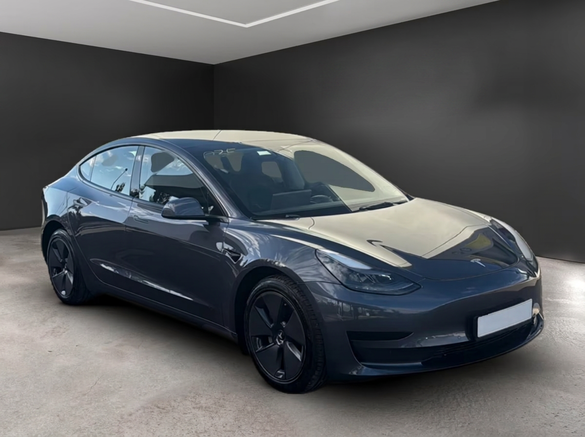 Front three-quarter view of the grey Tesla Model 3 in a dark showroom.