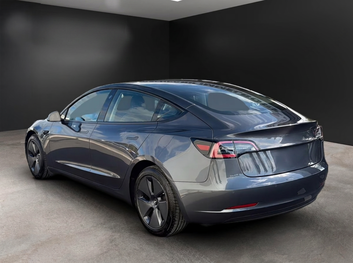 Rear three-quarter view of the grey Tesla Model 3 showing the LED tail lights.