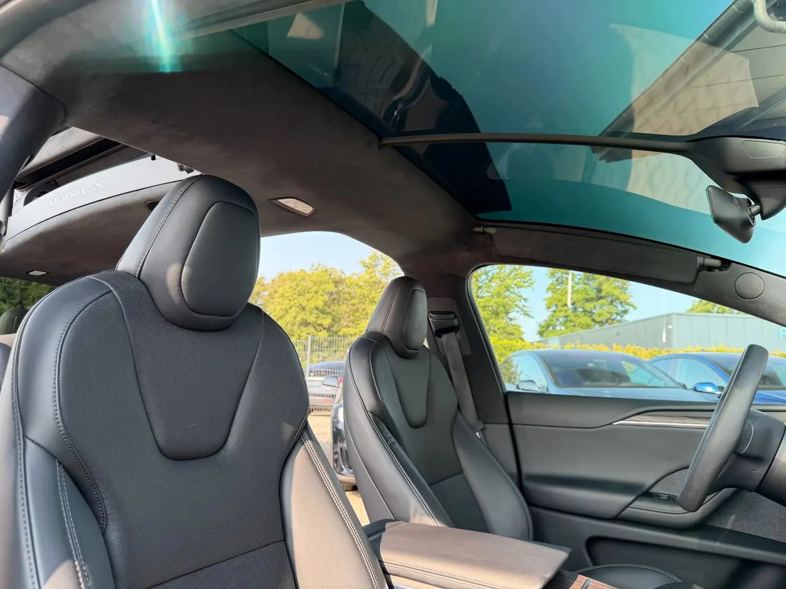 Black premium leather front seats of the Tesla Model X under the panoramic glass roof.